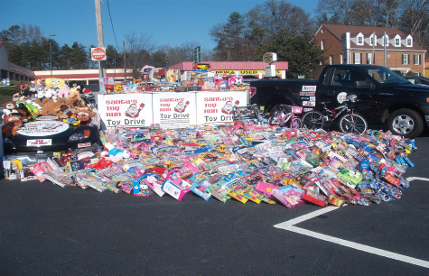Toys covering a parking lot in front of a black pickup and Toy Drive boxes